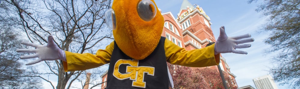 Yellow Jackets mascot, Buzz, standing in front of Tech Tower