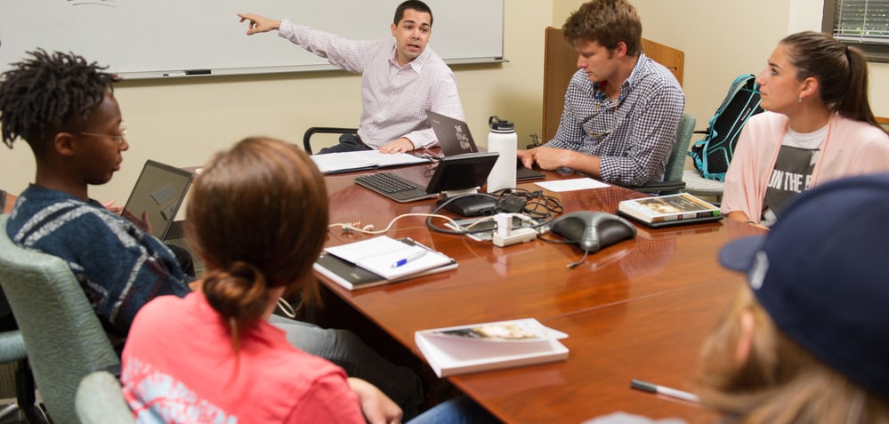 Professor pointing at the classroom whiteboard while lecturing to his class