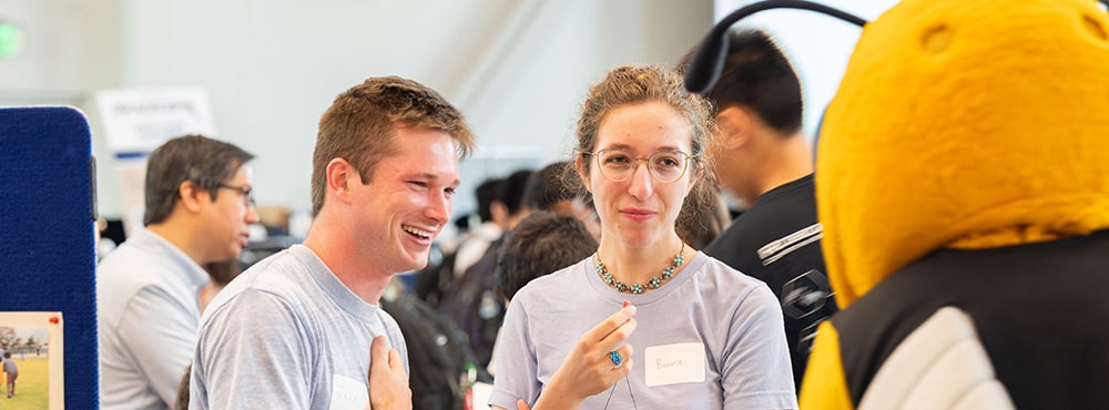 Graduate students talking with Buzz mascot